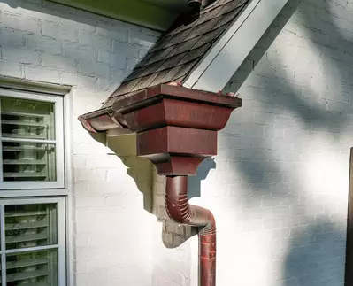 Copper half-round gutter system from GutterPro with collector heads installed on a white brick home.