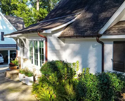 Copper half-round gutter system from GutterPro with collector heads installed on a white brick home.