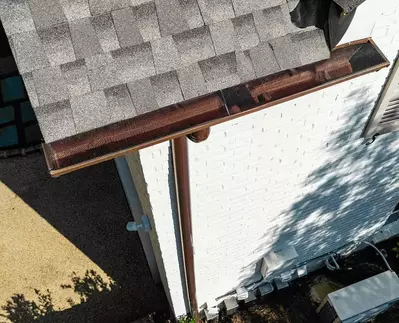Copper half-round gutter system from GutterPro with collector heads installed on a white brick home.