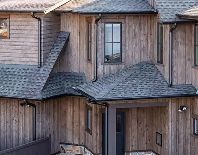 Sleek, black half-round gutters from GutterPro on wooden home facade that sits on the lakeside.