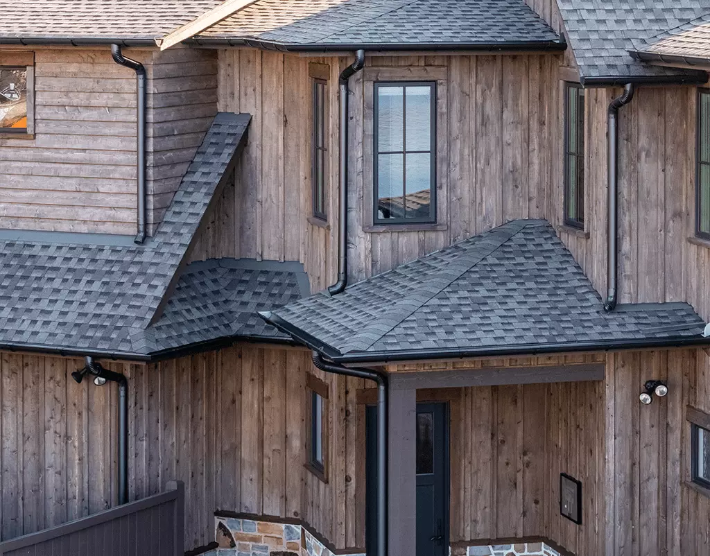 Sleek, black half-round gutters from GutterPro on wooden home facade that sits on the lakeside.