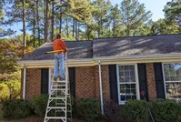man raking pine needles off roof of North Carolina home